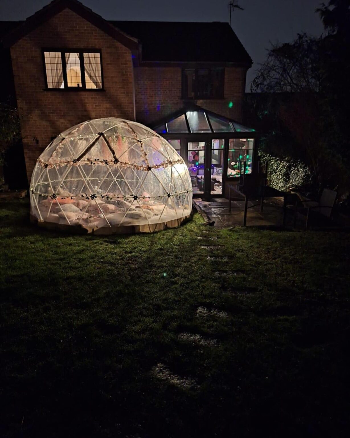 Igloo dome lit up at night in garden with house backdrop
